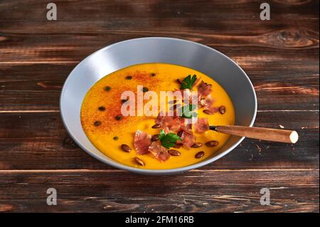 Traditional pumpkin puree cream soup with carrots, onions, ginger, garlic, coconut milk. Added seeds, fried bacon, parsley. Healthy, vegetarian food. Close up Stock Photo