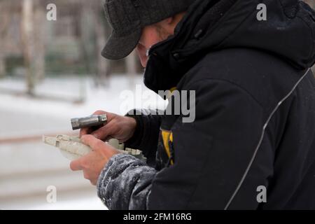 A worker in winter overalls repairs a chainsaw outdoors Stock Photo