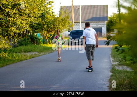 Defocus happy children playing on skateboard in the street. Caucasian kid riding penny board, practicing skateboard. Childhood and friendship concept Stock Photo