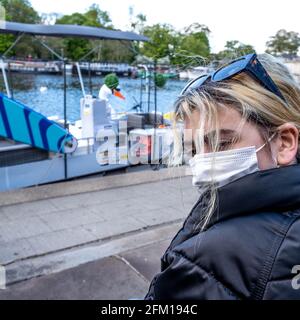 Kingston Upon Thames London UK, May 04 2021, Young Woman Sitting Alone On The Bank Of The River Thames Wearing A Protective Face Mask Or Covering Stock Photo