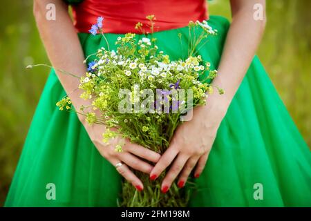 Girl in green dress with red manicure holds a field wild bouquet of summer flowers. Close up. Summer time. Summer mood concept. High quality photo Stock Photo