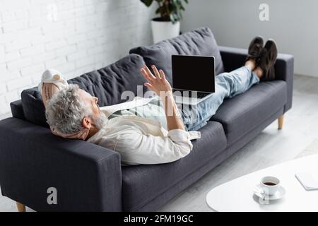 tattooed man having video call on laptop while lying on couch at home Stock Photo