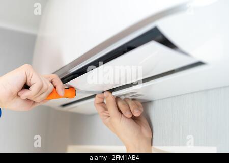 Close up of a repairman's hands with a screwdriver repairing an air conditioner on the wall Stock Photo