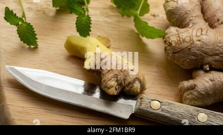 Cutting and slicing fresh ginger root pieces on the wooden cutting board with a vintage knife. Close up, macro. Stock Photo