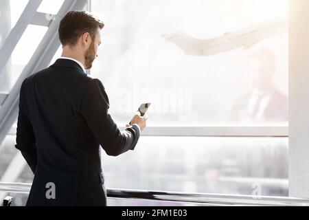 Back view of middle-aged entrepreneur going for departure, checking phone Stock Photo