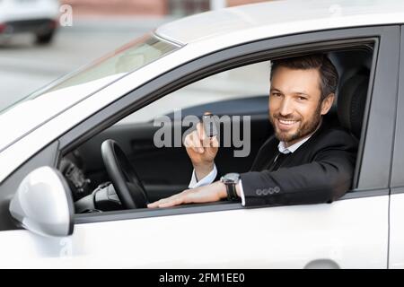 Cheerful businessman sitting in car, showing key Stock Photo