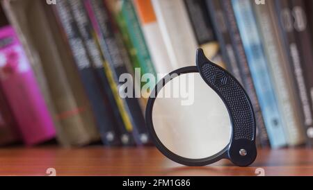 Magnifying glass on a bookshelf, background with books Stock Photo