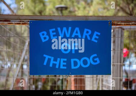 Beware of the dog, Warning messagel, text on blue sign. Label on metal rusty wire mesh fence background inform about caution, danger canine attack, at Stock Photo