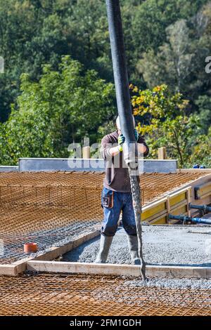 Pouring of concrete in rebar mesh for floors. Process of buiding new house. Construction worker holding pipe of pump machine while concreting ceilings. Stock Photo