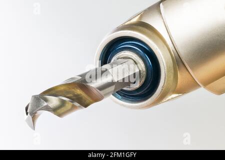 Closeup of drill bit tip clamped in chuck of right angle drilling head on a white background. Sharp cutting tool in machine part detail. Metal working. Stock Photo