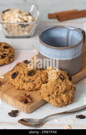Oatmeal and Raisins Cookies  on white background and decorated with spices, with empty tea or coffee cup and ingredients displayed in glass bowl Stock Photo