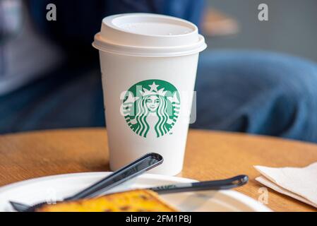 BERLIN - MAY 02: White paper cup with modern Starbucks logotype on a table at the Starbucks cafe in Berlin, May 02. 2021 in Germany Stock Photo