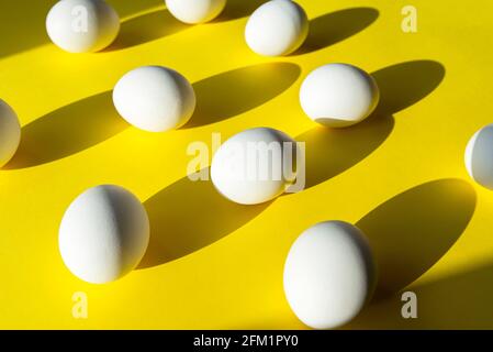 Many eggs on yellow surface, creativity picture with white  chicken egg, abstract composition with light and shadows Stock Photo