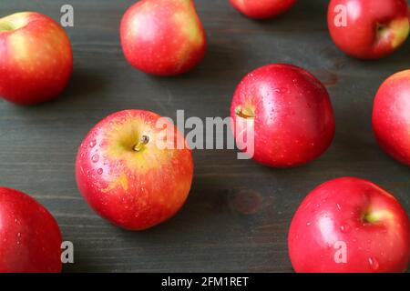 Closeup red fresh ripe apples with water droplets scattered on dark brown wooden table Stock Photo