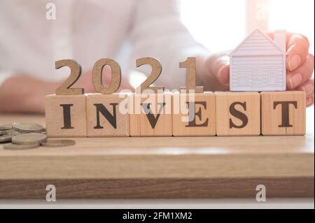 Investing in 2021 concept. Property investment and house mortgage financial concept, Word INVEST and 2021 on wood cubes and miniature house on wood ta Stock Photo