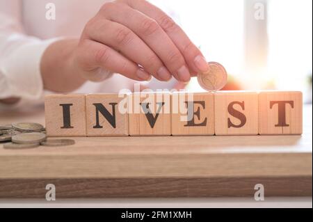 Word INVEST on wood cubes and hand holding euro coin. Investment concept.