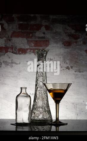 Glass vase, jar and glass with the yellow beverage on it in front of the bricks background. Still Life image. Stock Photo