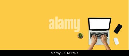 Hand using computer laptop and mouse, phone from above on yellow background. Stock Photo
