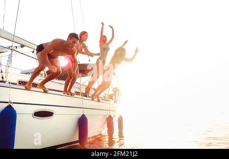 Side view of young crazy friends jumping from sailboat on sea ocean trip - Men and women having summer fun together at sail boat party day - Luxury ex Stock Photo