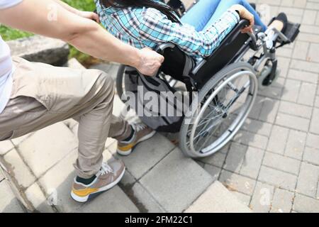Man lifts a woman in wheelchair up stairs Stock Photo
