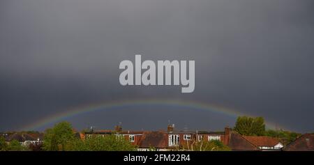 Wimbledon, London, UK. 5 May 2021. Afternoon skies darken dramatically as a band of heavy rain sweeps over London, a low rainbow forms as the storm passes. Credit: Malcolm Park/Alamy Live News. Stock Photo