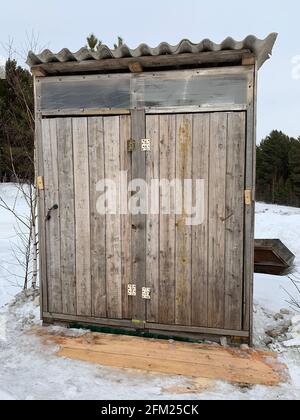 Wooden outdoor toilet for two in the countryside in winter, in nature or a tourist destination. An old but working toilet for people. Stock Photo