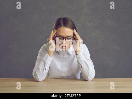 Tired woman office worker or teacher suffering from headache sitting at desk Stock Photo