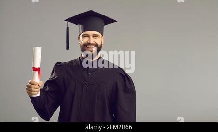 Portrait of a smart and successful male graduate with a diploma in his hands on a gray background. Stock Photo