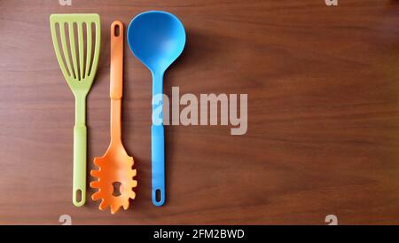 3 colorful kitchen utensils arranged neatly side by side on a wooden surface, with copy space on the right.
