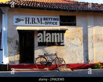 A bicycle rests in front of an old, worn, classic H.B.M. Betting Office building in the historic city center. In Galle, Sri Lanka Stock Photo