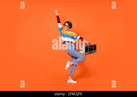 Photo of charming young woman wear striped sweater eyewear dancing holding boombox isolated orange color background Stock Photo