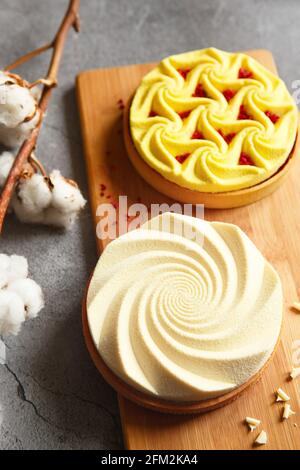 Delicious mini tarts yellow and white with nuts and custard on wooden cutting board. Assortment of delicious and colorful dessert, lemon curd tart, cr Stock Photo