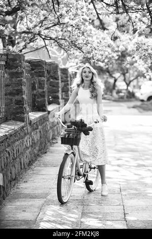 Spring style travel. retro woman sell tulip flower bouquet. girl under sakura with vintage bicycle. spring beauty and fashion. cherry tree pink Stock Photo