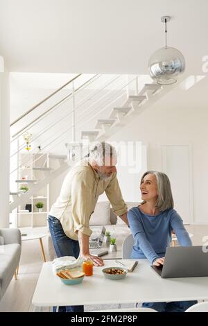 Happy middle aged couple using laptop computer and talking at home. Stock Photo