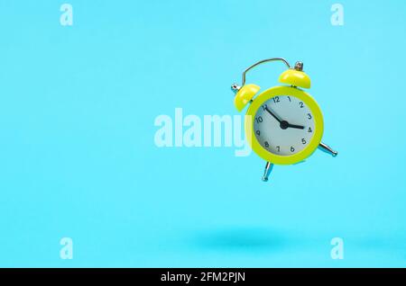 Yellow retro alarm clock levitates. Alarm clock in the old style on a blue background. 15-55 pm. The concept of the seven hour working day Stock Photo