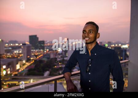 Portrait of handsome African businessman outdoors at rooftop in Bangkok, Thailand Stock Photo