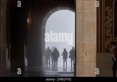 Domestic and International tourists wearing facemarks are visiting the monastery of Montserrat during a misty and rainy spring day, at the end of the pandemic induced Spanish State of Emergency in the Montserrat mountain range, west of Barcelona in the province of Catalonia, Spain. © Olli Geibel Stock Photo