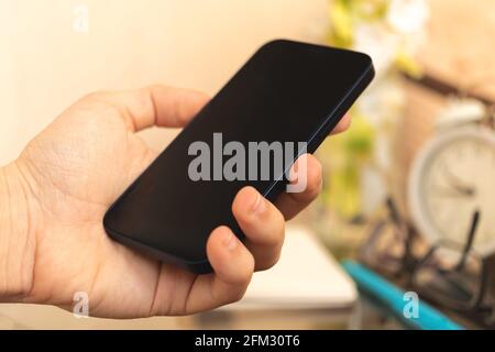Man hold black smartphone on home interior background, concept of using mobile phone Stock Photo