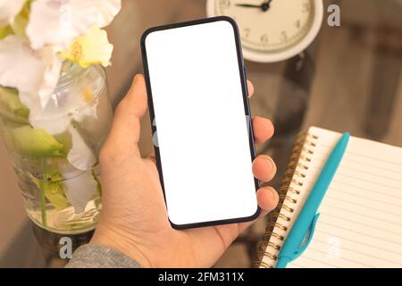 Fashion mobile screen mockup, background of notebook, pen and alarm clock on office desk, man hold smartphone with blank white screen Stock Photo