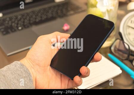 Man uses smartphone on home interior background with laptop, blank screen mockup concept Stock Photo
