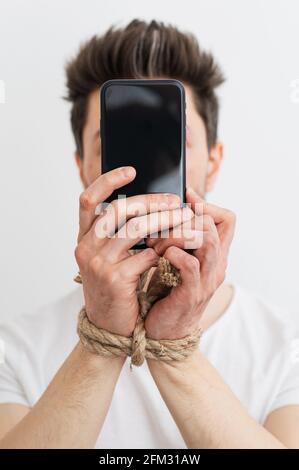 a person with his hands tied holding a smartphone, internet addiction, or social media addiction. Stock Photo