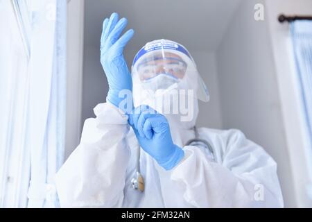 Doctor wearing PPE putting on surgical gloves, Thailand Stock Photo