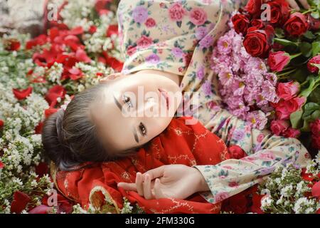 Beautiful woman lying in a meadow of flowers surrounded by roses Stock Photo