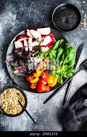 Bunch of purple basil, tomatoes and radishes on a plate with black sesame seeds and sunflower seeds Stock Photo