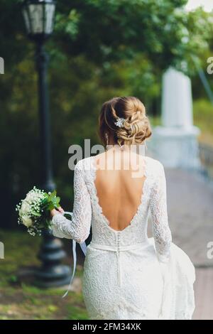 Bride in white dress holding a rose bouquet at the back Stock Photo