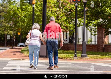 Senior caucasian couple in love holding hands as they cross the street on pedestrian crossing on a lovely spring day. Activity, togetherness at elderl Stock Photo