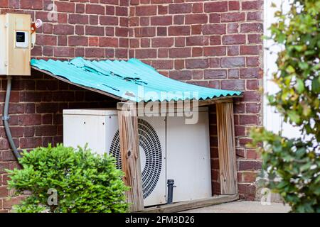 An outdoor air conditioner AC unit placed on the ground at a garden within a small protective utility shed with corrugated painted metal roof. This pr Stock Photo