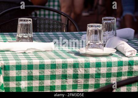An outdoor table at a restaurant at lunch time with no customers around. Glass cups are put upside down on plates to avoid dust coming in. Cutlery is Stock Photo