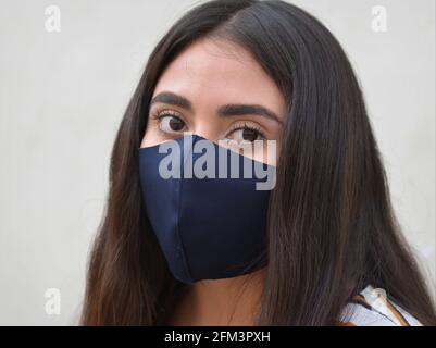 Young Caucasian Latina woman with big brown eyes and long hair wears a black non-medical washable face mask during the global coronavirus pandemic. Stock Photo