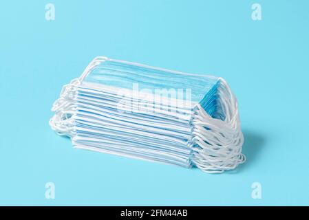 Pile of medical face masks on a blue table. Stack of surgical masks isolated on a blue-colored background. Coronavirus protection supplies. Stock Photo